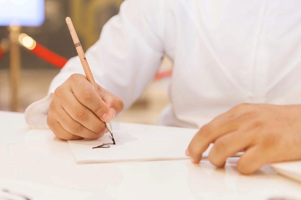 Man creating calligraphy art on a white piece of paper, hands in frame