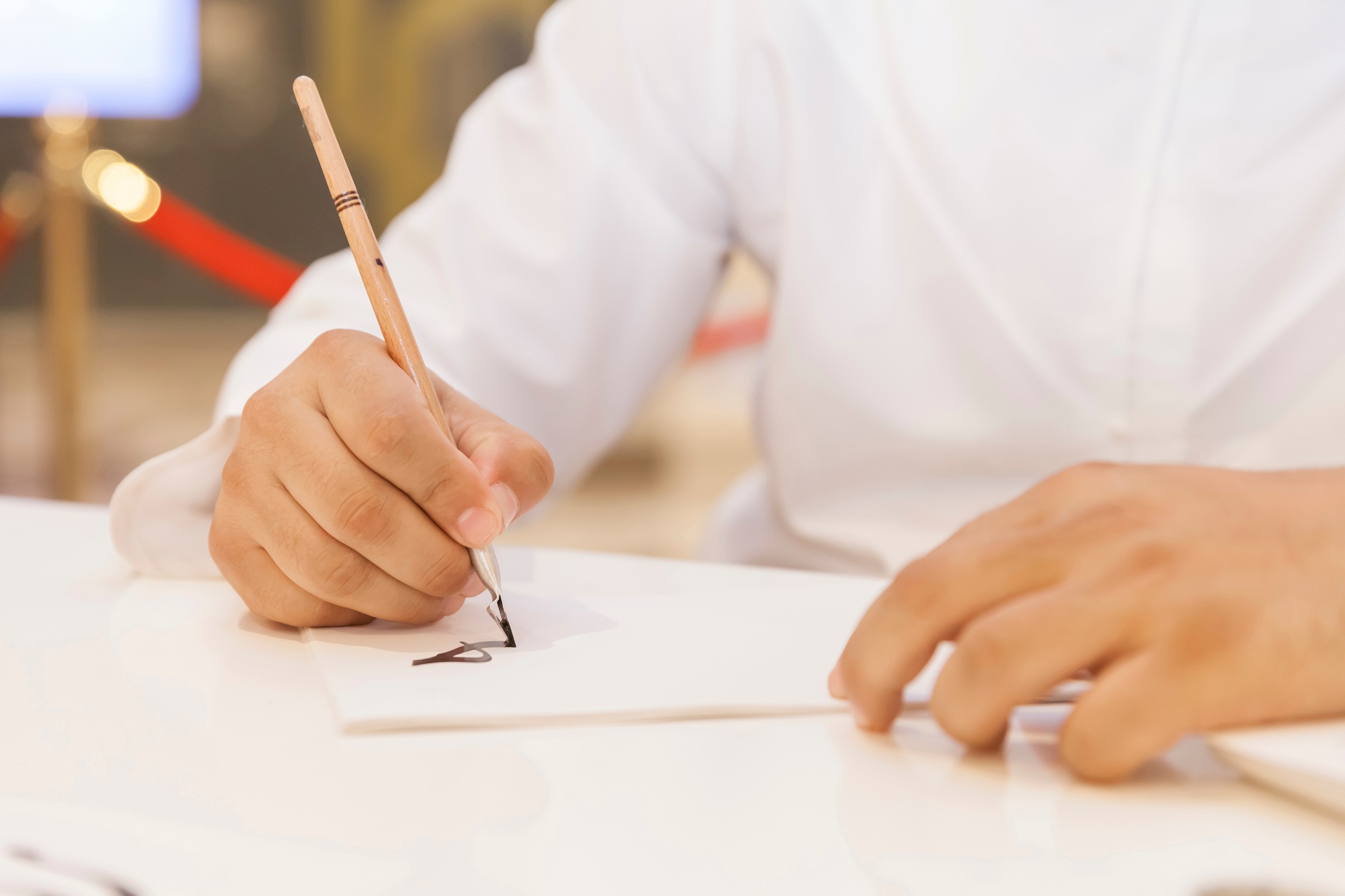 Man creating calligraphy art on a white piece of paper, hands in frame