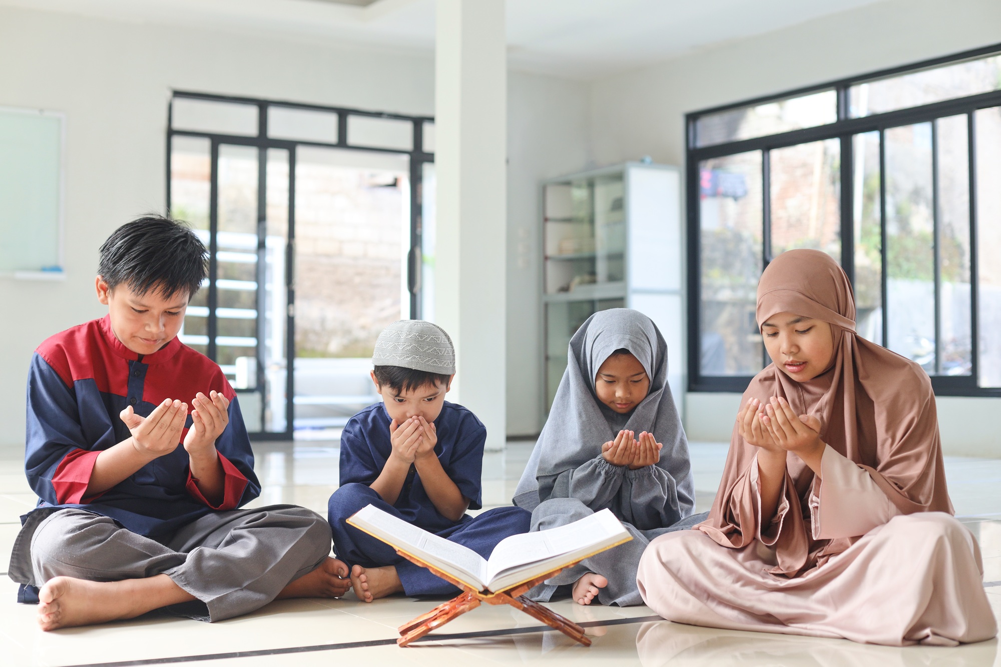 Portrait of muslim kids praying with holy Quran