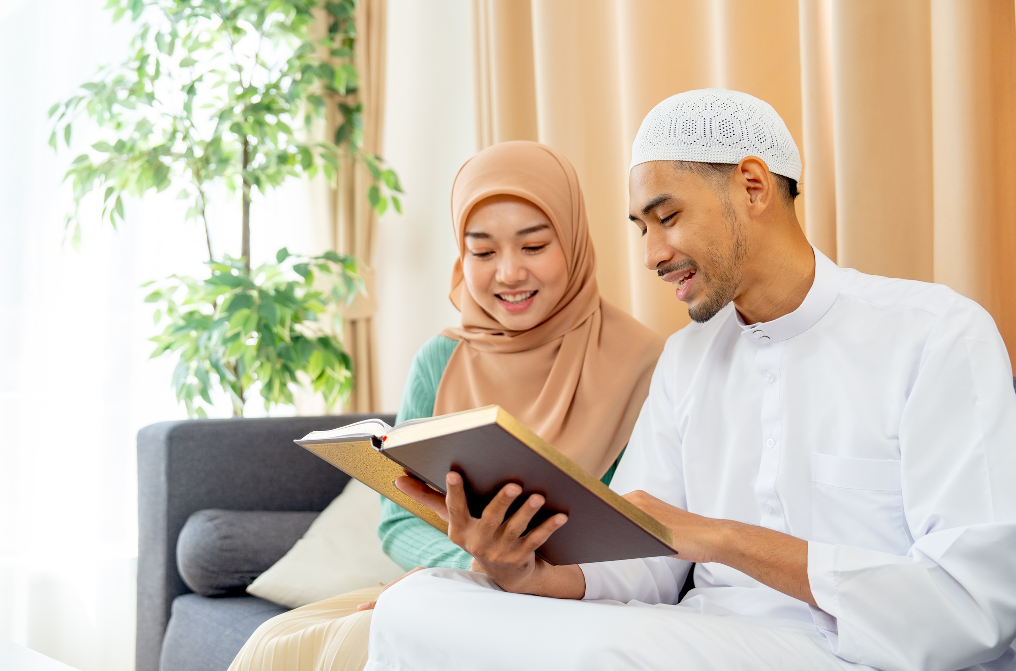 Side view of couple muslim man and woman sit on sofa and read islam teaching book together
